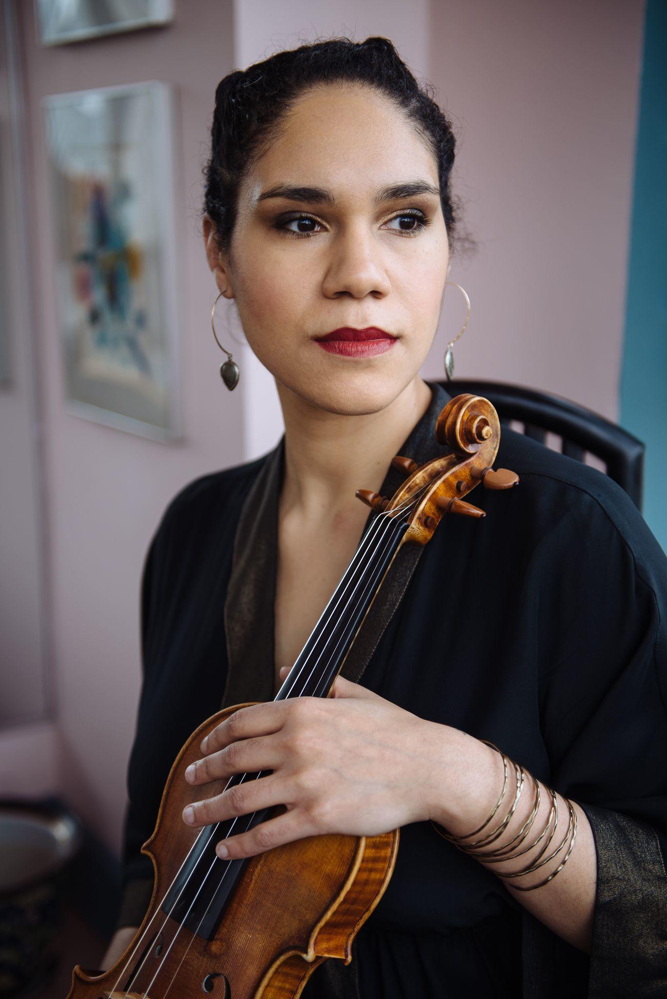 Photograph of composer, Jessie Montgomery, close up on face looking off into the distance., holding a violin