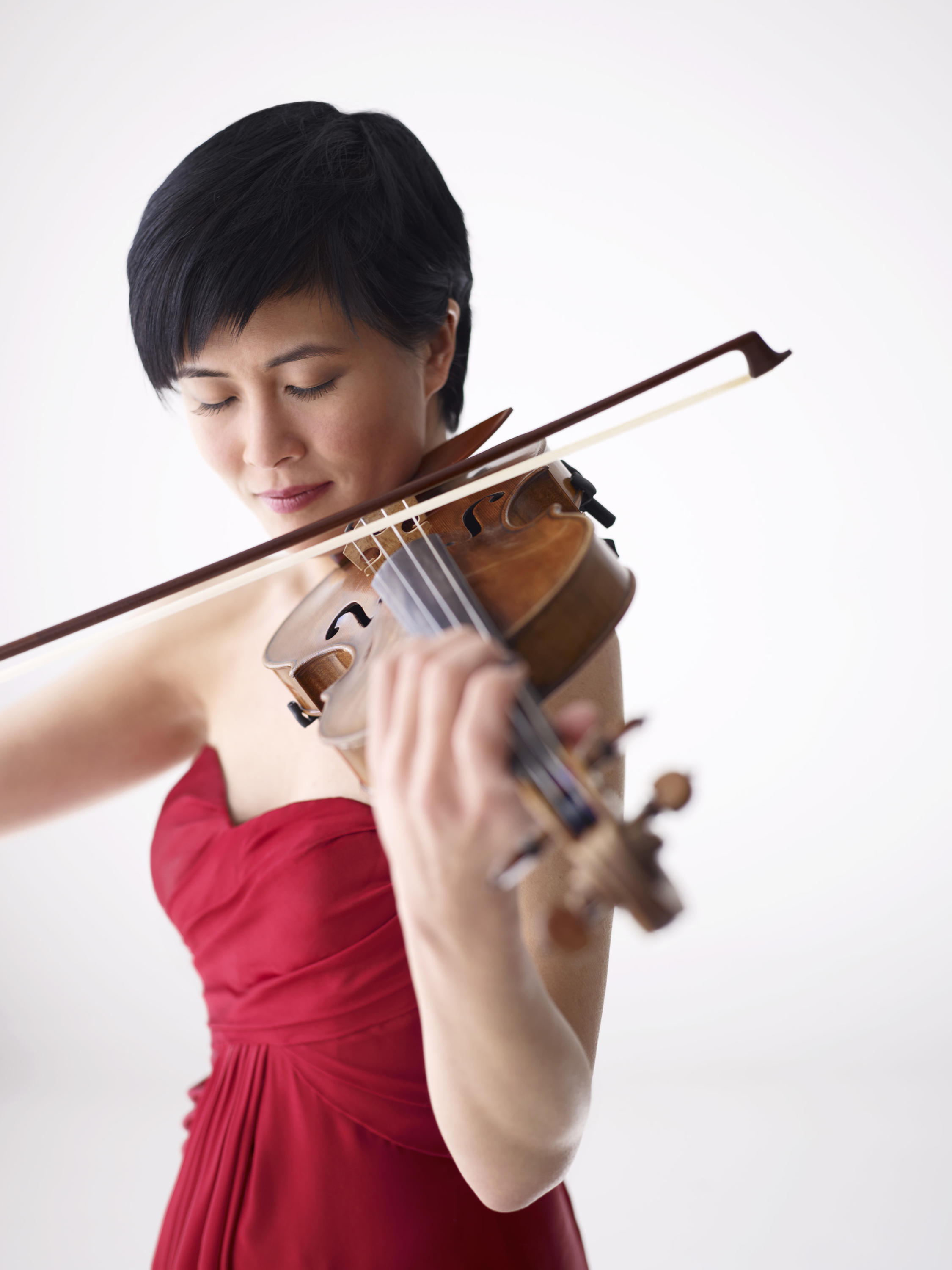 Eyes closed, violinist Jennifer Koh plays her violin. She wears a red formal gown.