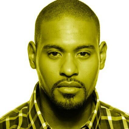 A headshot of Dennis Allen. He gazes at the camera with a neutral expression. He wears a plaid button up shirt. The photo is overlaid with a green-yellow hue.